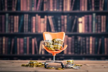 Kleiner Plastikstuhl, der mit Münzen übersät ist und vor einer Bücherwand steht