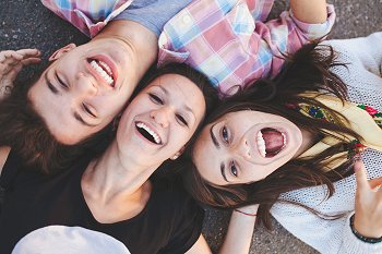 Drei Studenten liegen lachend auf dem Boden und schauen in die Kamera