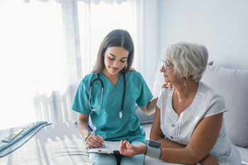 Eine Physician Assistant sitzt mit einer Patientin am Krankenhausbett und führt mit ihr die Visite durch