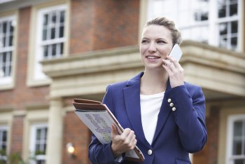 Immobilienmaklerin steht telefonierend vor einem Haus
