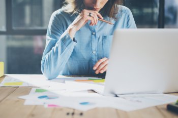 Studentin sitzt mit Grafikcharts und Unterlagen an Laptop